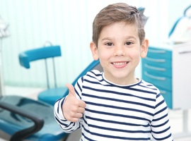 A little boy wearing a striped shirt and giving a thumbs up after completing a fluoride rinse