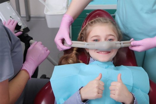 Girl giving two thumbs-up as dentist administers laughing gas