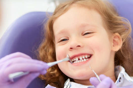 Pediatric dentist examining a young girl’s teeth as she smiles