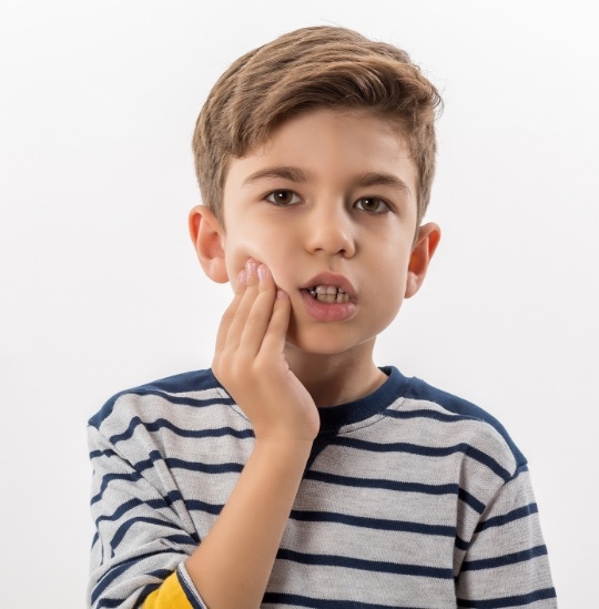 Boy holding his cheek in pain needing pediatric emergency dentist