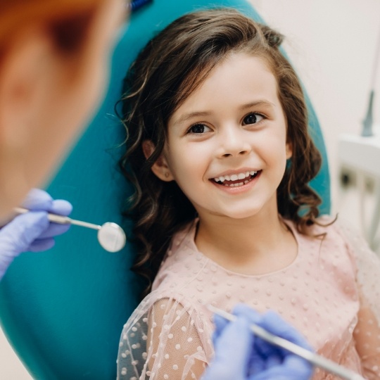 Young girl in dental chair smiling at her dentist