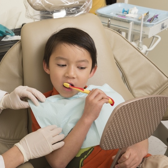 Boy in dental chair brushing his teeth in front of mirror
