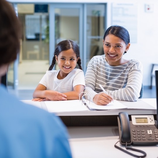 Mother and daughter smiling at dental office receptionist