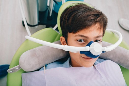 : Boy wearing a nitrous oxide nasal mask smiling in patient’s chair
