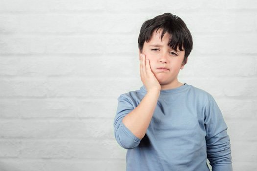 Boy rubbing his aching jaw on white brick background 