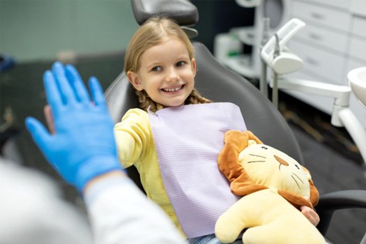 Little girl in dental chair holding stuffed lion high-fiving dentist