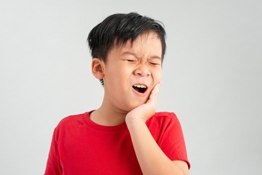 Little boy in red shirt holding hand to jaw in pain
