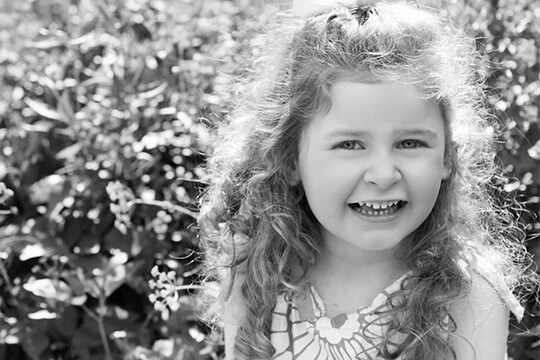 Girl with curly hair smiling next to a bush