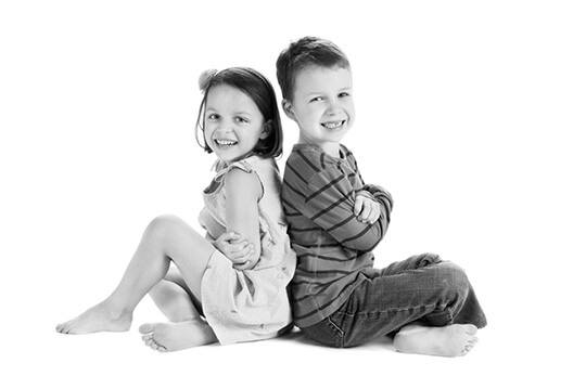 Boy and girl sitting back to back on white floor