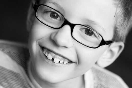 Boy with glasses smiling with a few missing teeth