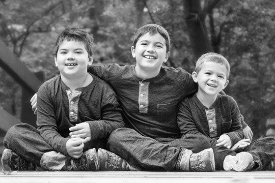 Three smiling boys sitting on sidewalk