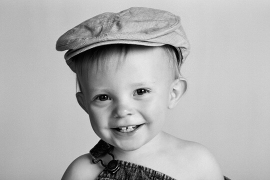Young boy smiling in overalls and newsboy cap