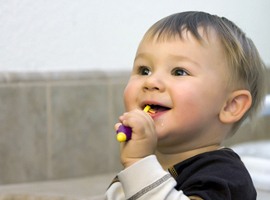 A baby smiling while brushing its teeth with a manual toothbrush