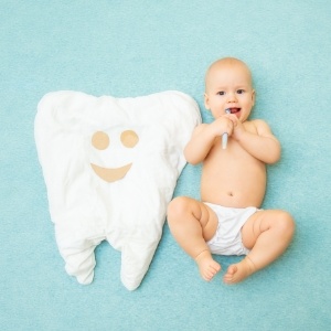 Baby holding toothbrush and laying on their back next to tooth shaped blanket