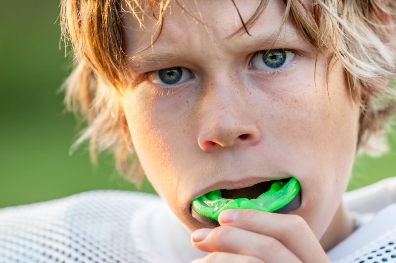 a young boy wearing football gear and preparing to insert a customized mouthguard to protect his teeth and gums