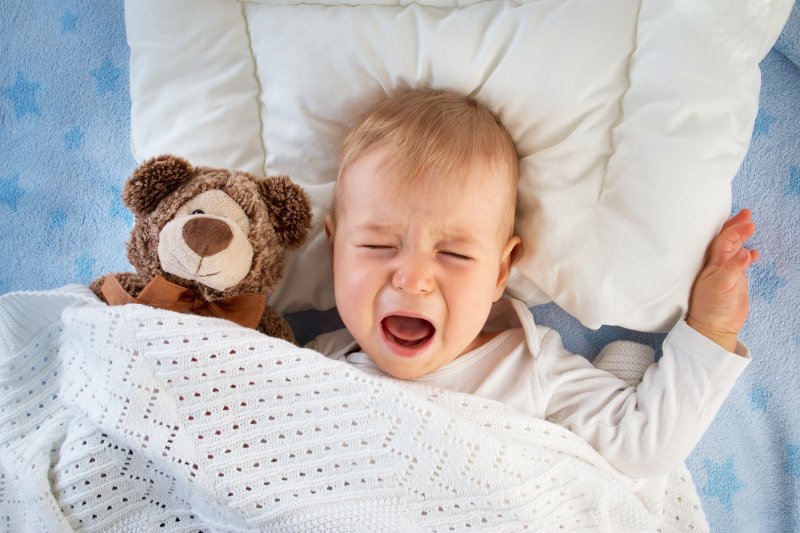 a baby lying in bed holding a teddy bear and teething in Hinsdale