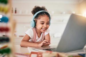 a child smiling and doing schoolwork on a laptop