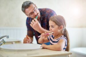 a father brushing his teeth with his young daughter