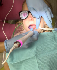 a child in a dental chair with glasses on while a pediatric dentist is working in their mouth